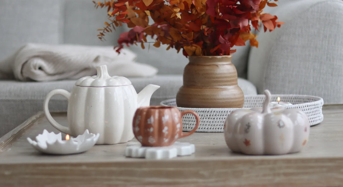 Autumn collection table setting with ceramic pumpkins, teapot, and fall foliage.