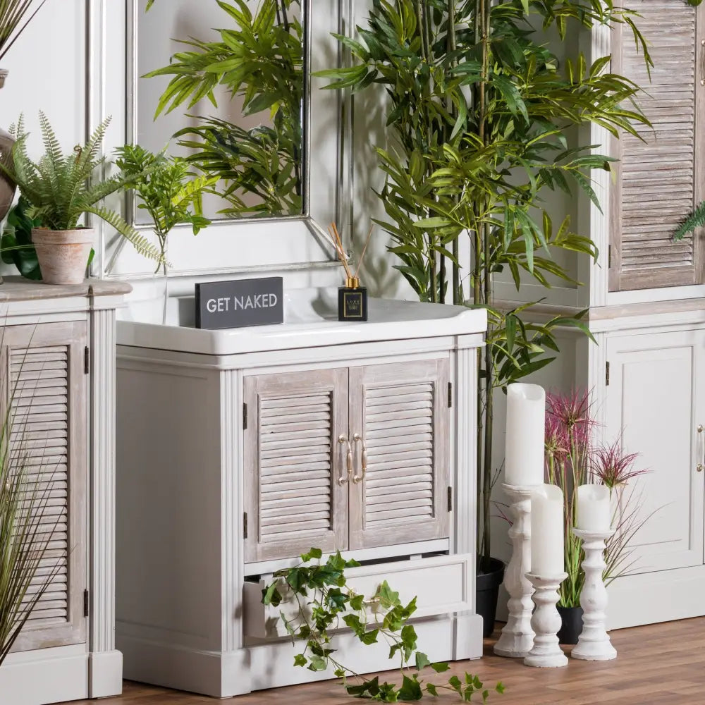 White wooden cabinet with louvered doors and a Get Naked sign atop a stone candle holder