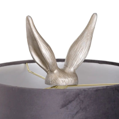 Rabbit ears peek out of a dark container in a Silver Hare Table Lamp with Grey Velvet Shade