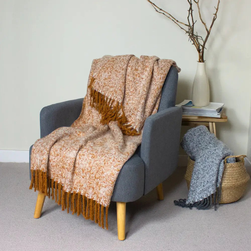 Gray armchair with wooden legs and a beige throw in herringbone design